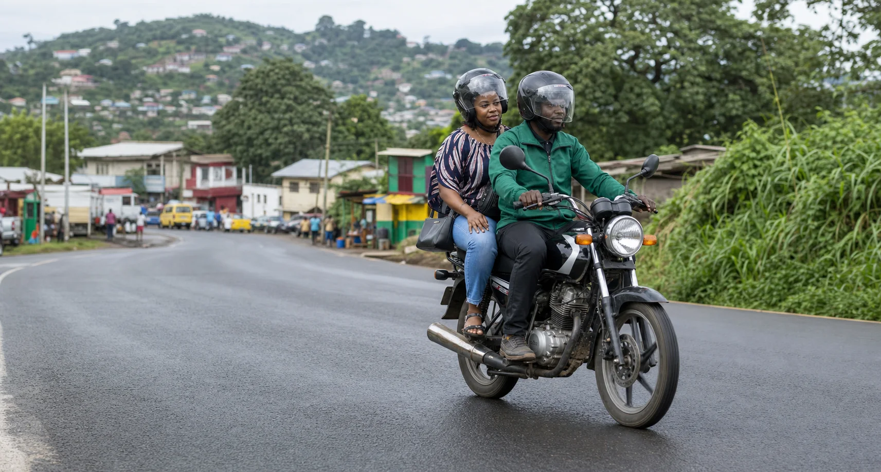 A MeRide motorbike rider safely transporting a passenger on a road in Freetown